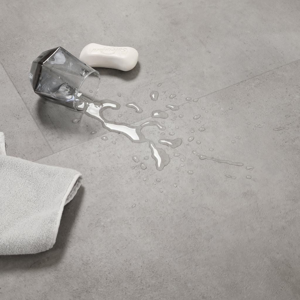 Wasserfestigkeit-Test Ravenna Grau Vinylboden – umgekipptes Wasserglas mit Wassertropfen auf dem Boden, demonstriert 100% Wasserfestigkeit und Feuchtraumeignung von Floor4all