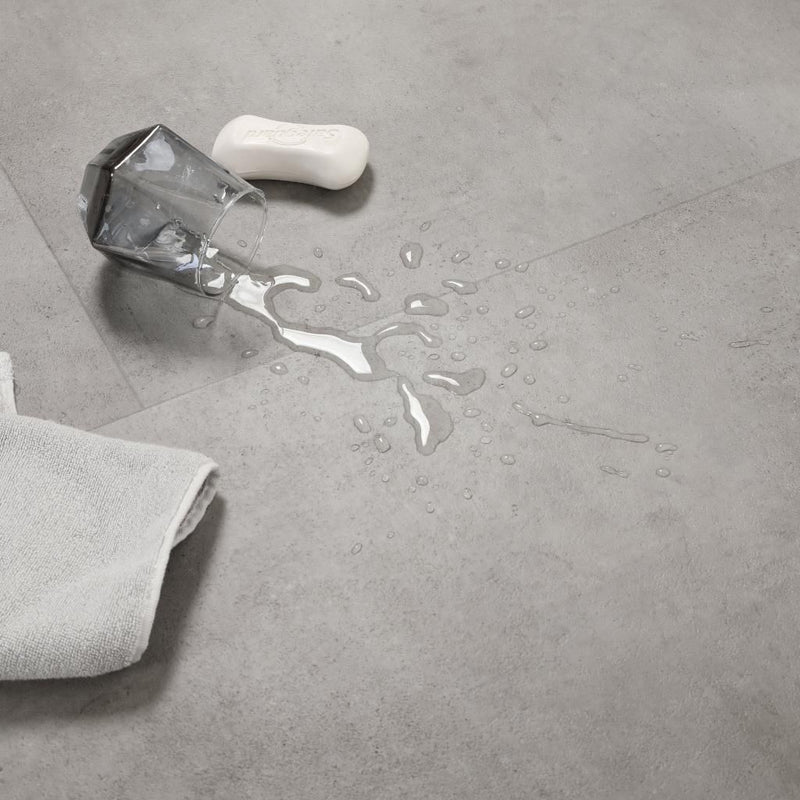 Wasserfestigkeit-Test Ravenna Grau Vinylboden – umgekipptes Wasserglas mit Wassertropfen auf dem Boden, demonstriert 100% Wasserfestigkeit und Feuchtraumeignung von Floor4all