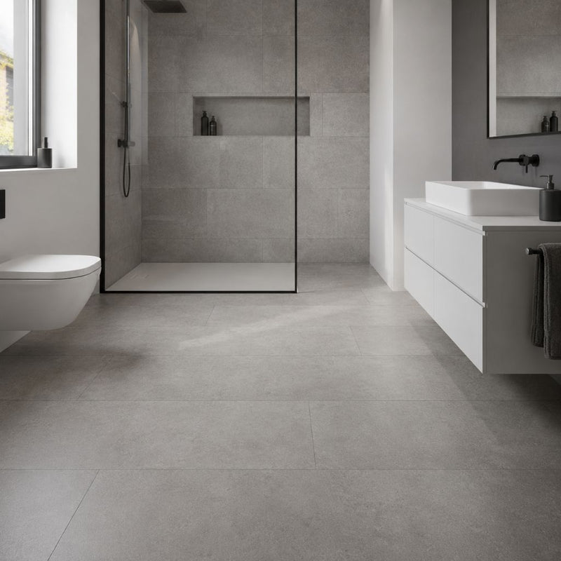 Modernes Badezimmer mit Ravenna Grau Vinylboden in Fliesenoptik – große graue Fliesen mit authentischer Textur, begehbare Dusche mit Glastrennwand, weißes Waschbecken, elegantes Design von Floor4all