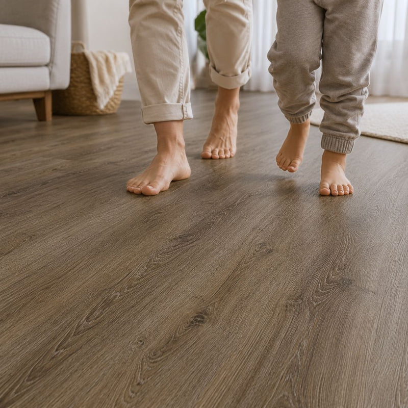 Zwei Personen und ein Kind gehen barfuß über den Vinylboden River Oak Brown, demonstriert die Begehbarkeit, Fußwärme und Komfort des Belags in einem hellen Wohnzimmer - Floor4all